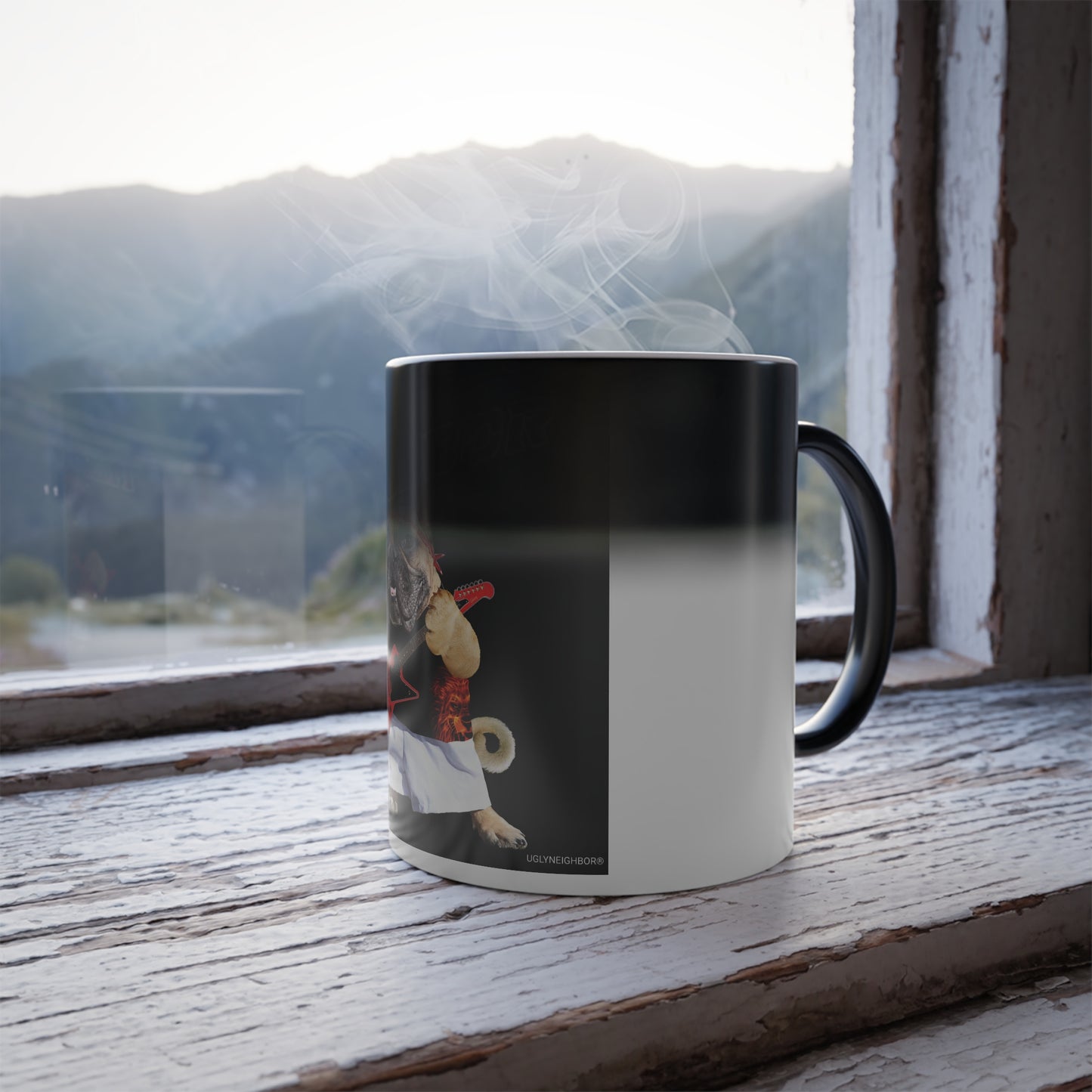 A ceramic mug with a black handle and a black-to-white gradient design, sitting on a rustic wooden windowsill with a mountain landscape visible outside.