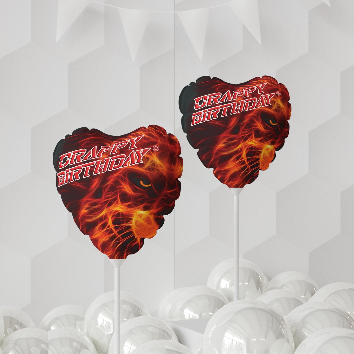 A Mylar balloon with a fiery design and the text 'CRAPPY BIRTHDAY' displayed on top, placed on a table with gift boxes and surrounded by plants.
