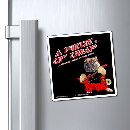 A square refrigerator magnet with a black background and a cartoon dog wearing red shorts, attached to a brushed stainless steel refrigerator door next to the handle.