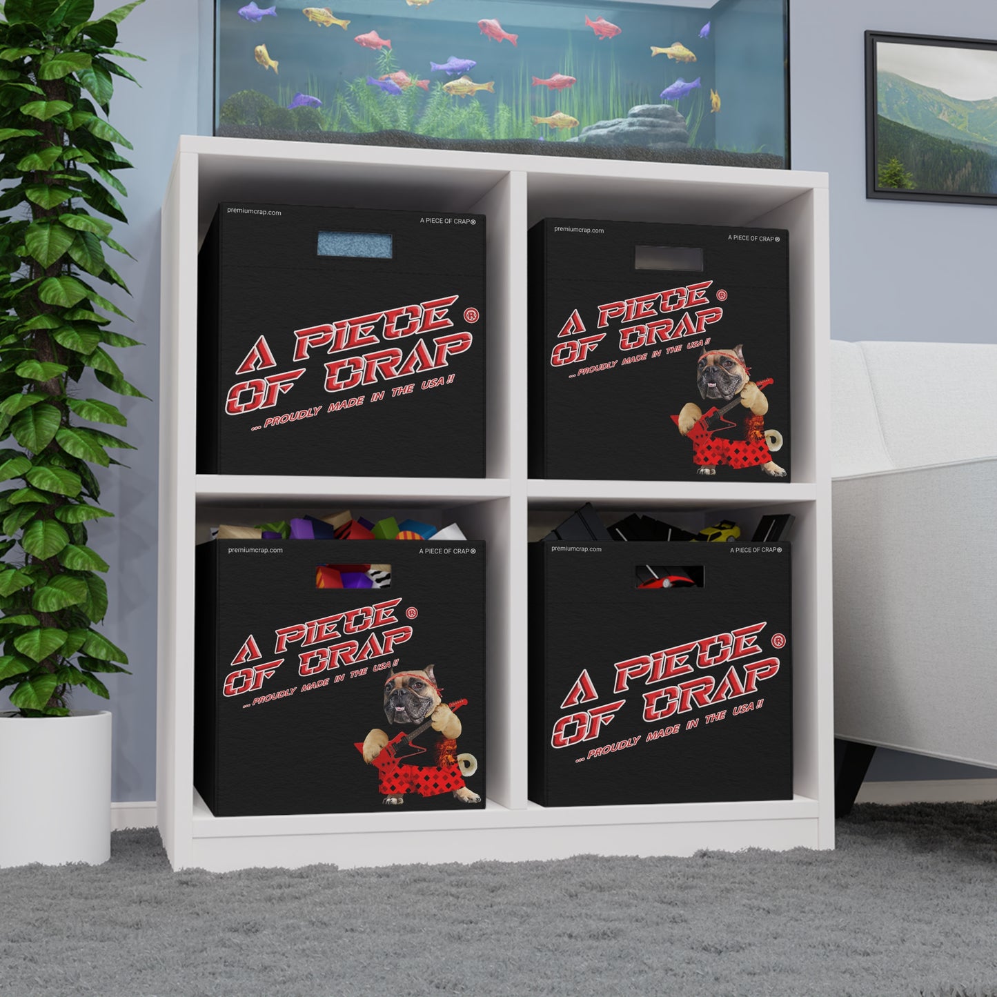 Four black storage bins with 'A Piece of Trap' graphics arranged inside a white four-compartment shelf, set in a room with a plant, aquarium, and sofa.