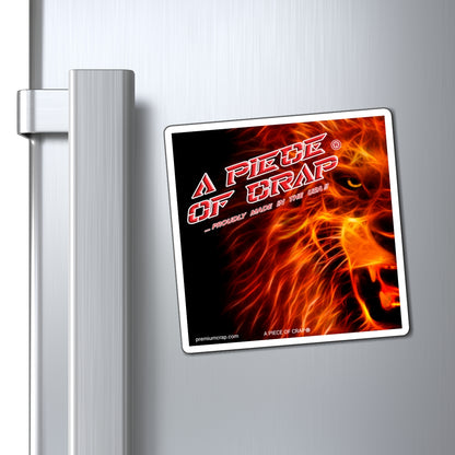 A rectangular refrigerator magnet with a white border, featuring a fiery lion graphic and the text 'A PIECE OF CRAP - PROUDLY MADE IN THE USA', shown attached to a brushed stainless steel refrigerator door next to the handle.
