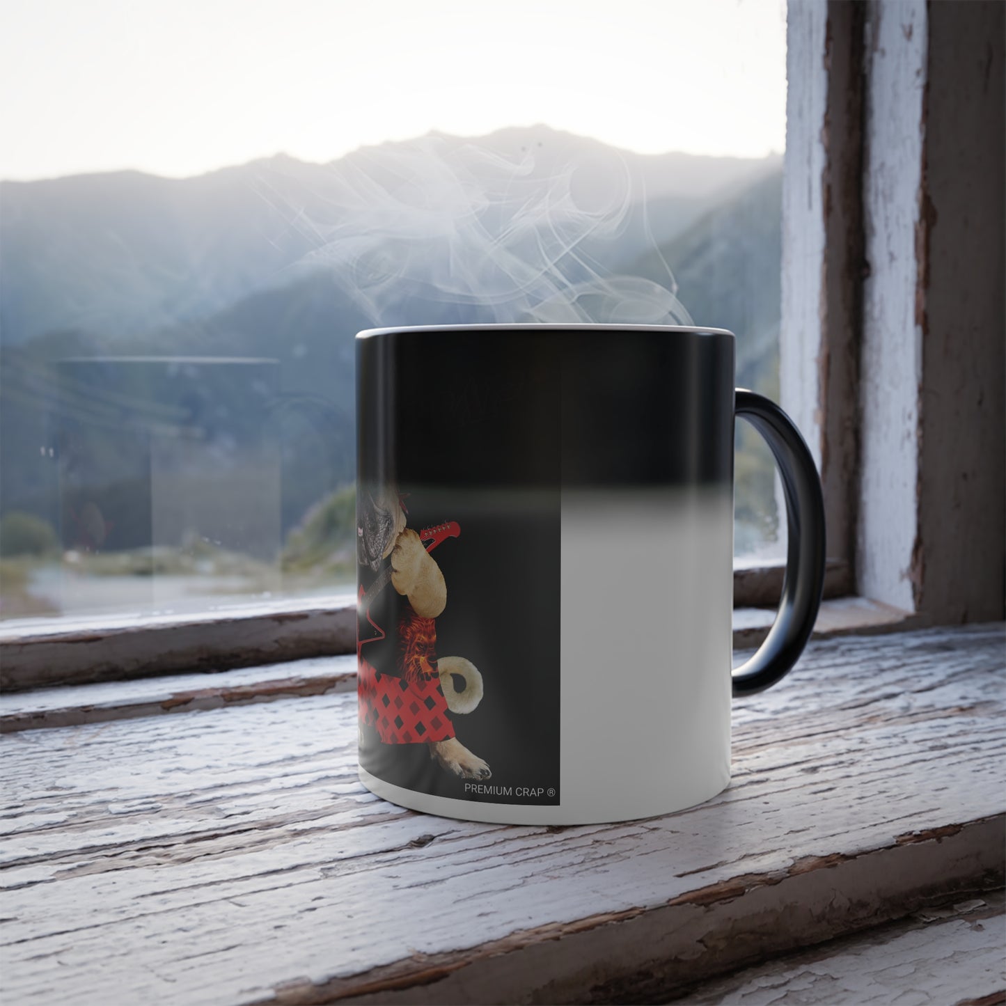 A ceramic mug with a black and white gradient design and a cartoon dog illustration, sitting on a rustic wooden windowsill with steam rising from the top, set against a blurred mountain landscape.