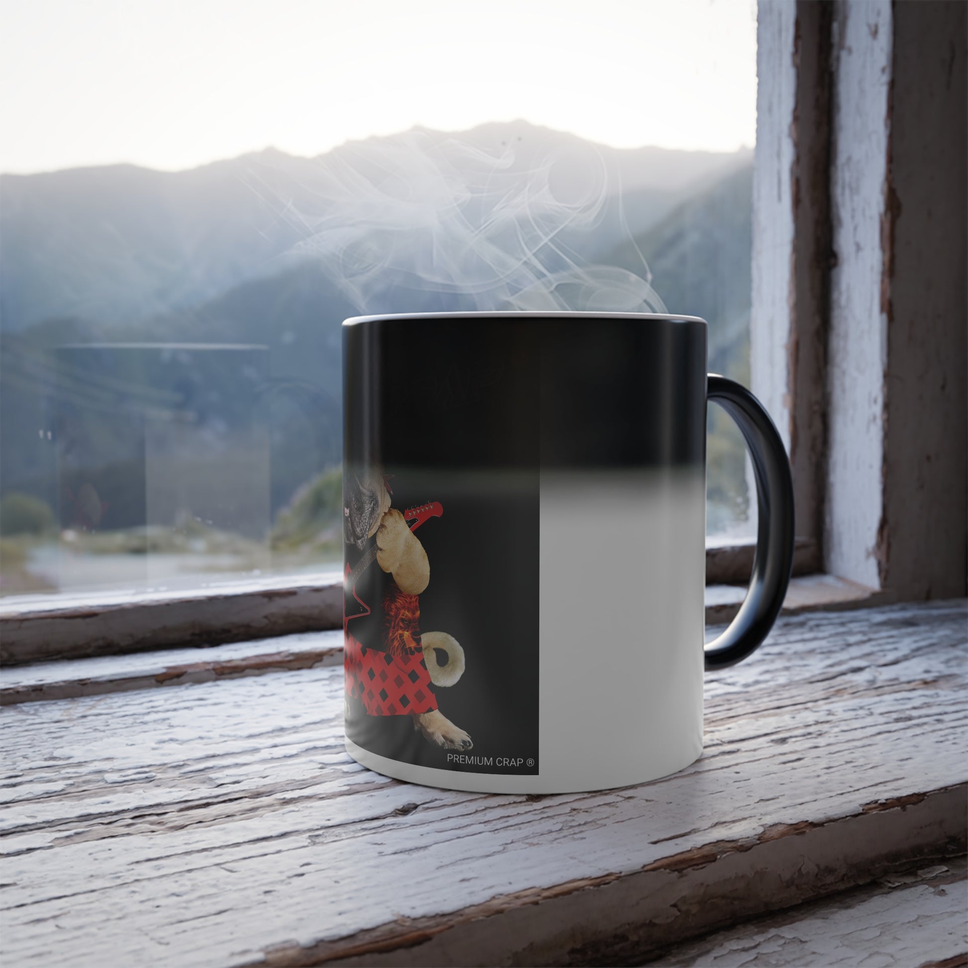 A ceramic mug with a black and white gradient design and a cartoon dog illustration, sitting on a rustic wooden windowsill with steam rising from the top, set against a blurred mountain landscape.