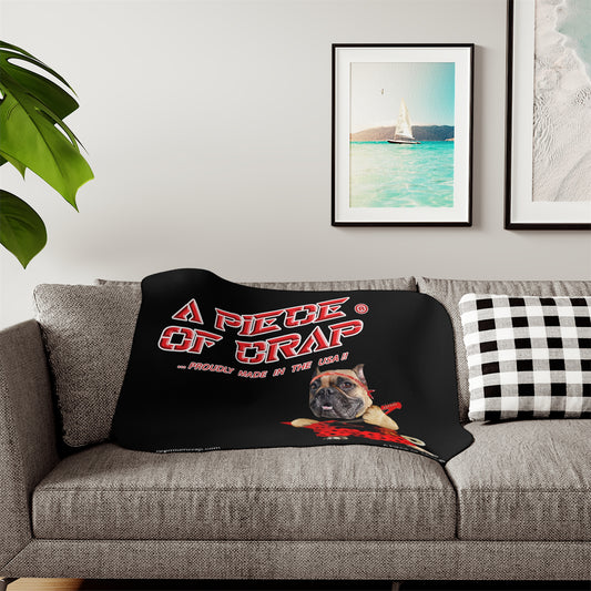 Black blanket with a dog graphic and text on a gray couch, with framed pictures on the wall.